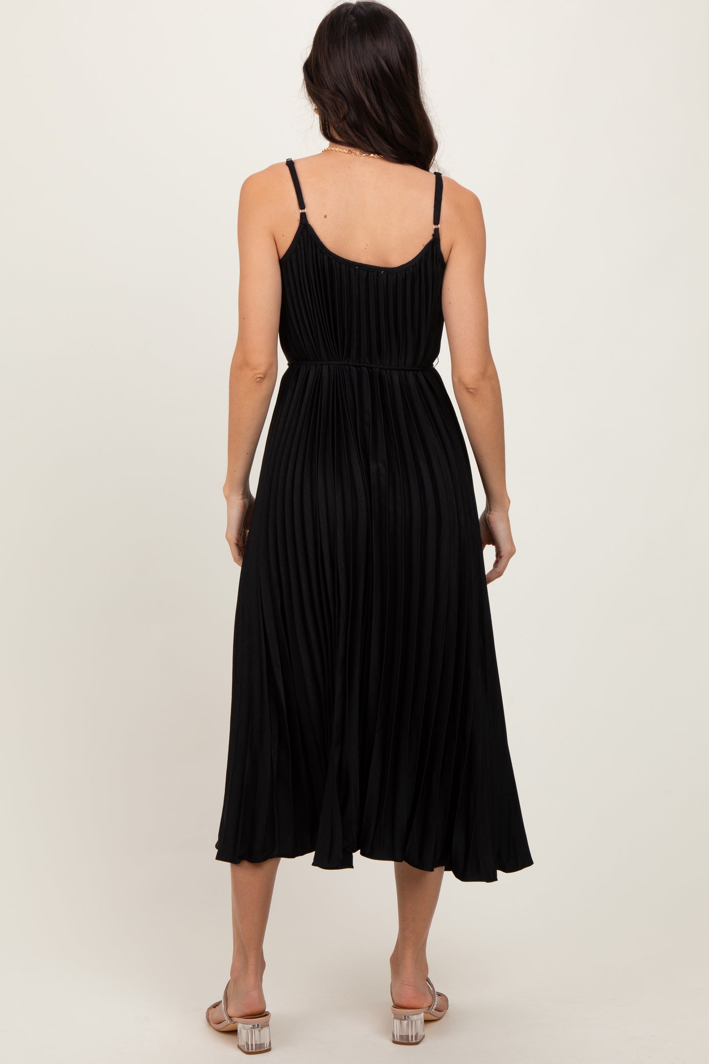woman wearing a black pleated midi dress with thin straps, showcasing the back view