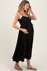 woman wearing a black pleated maternity dress with a tie waist, gently cradling her baby bump
