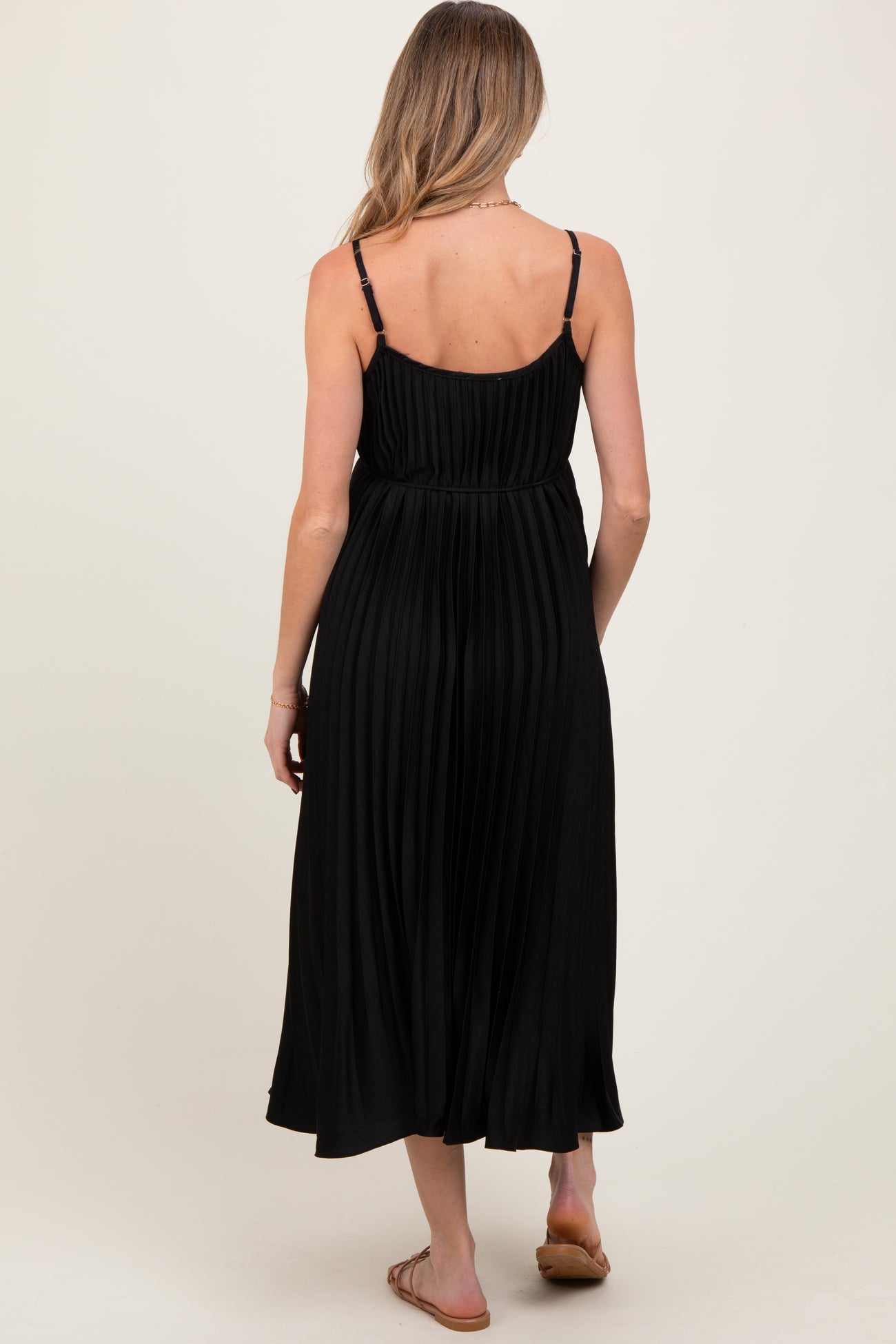 woman wearing a black pleated maternity dress with thin straps, showcasing the back view