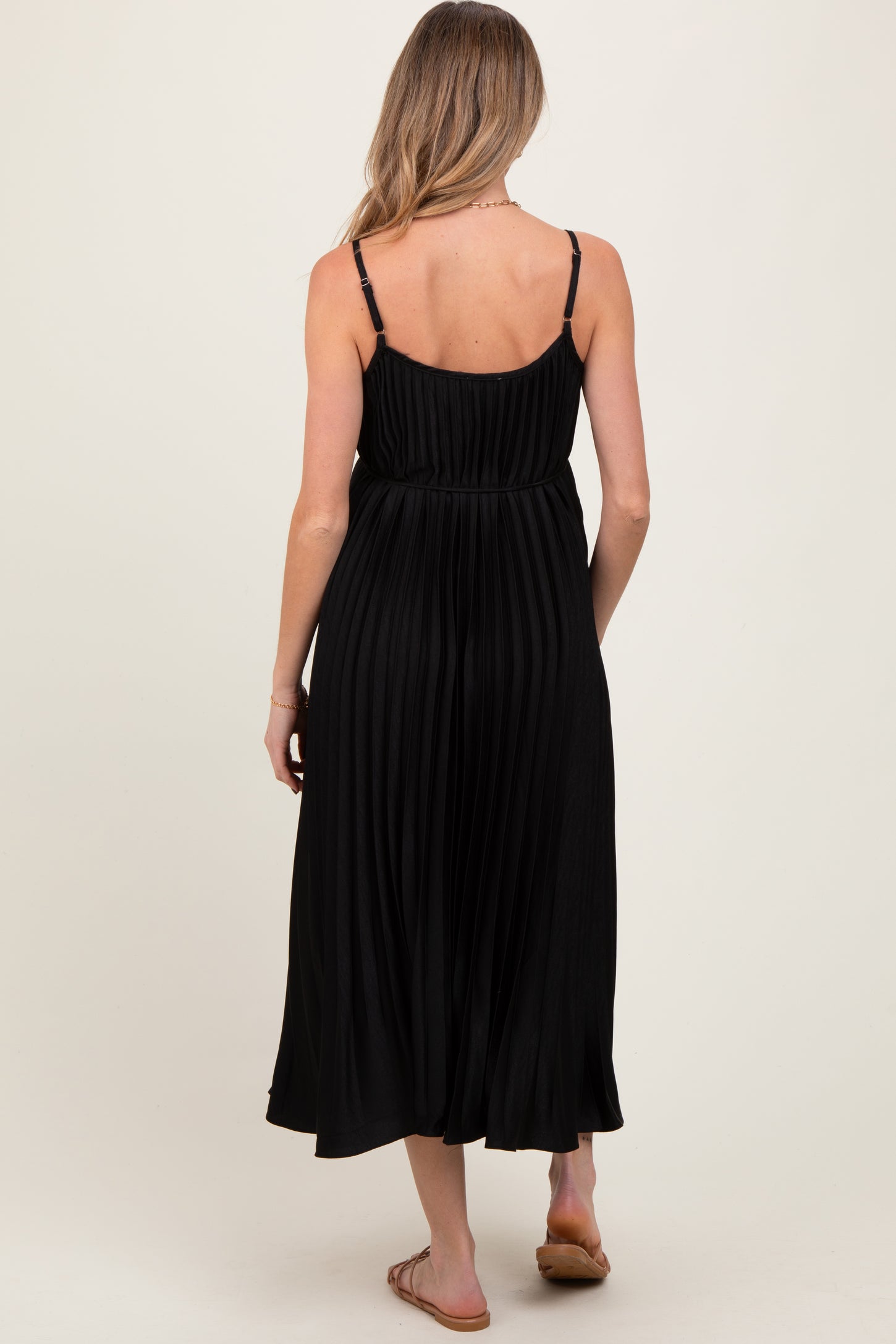 woman wearing a black pleated maternity dress with thin straps, showcasing the back view