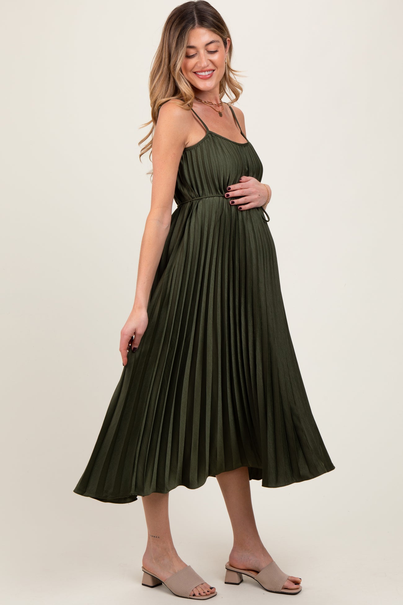 woman wearing a dark green pleated maternity dress with adjustable straps and a visible baby bump