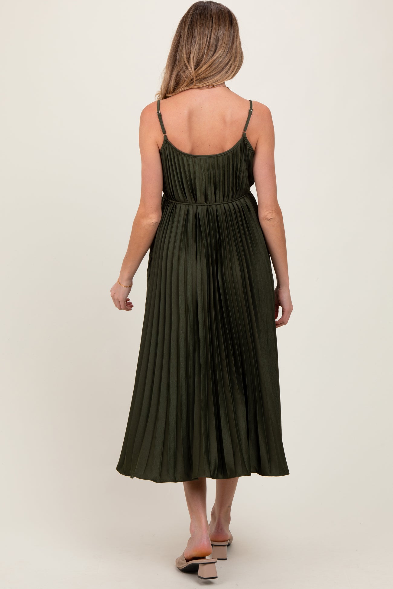 woman wearing a dark green pleated maternity dress with adjustable straps, view of back and flowing skirt