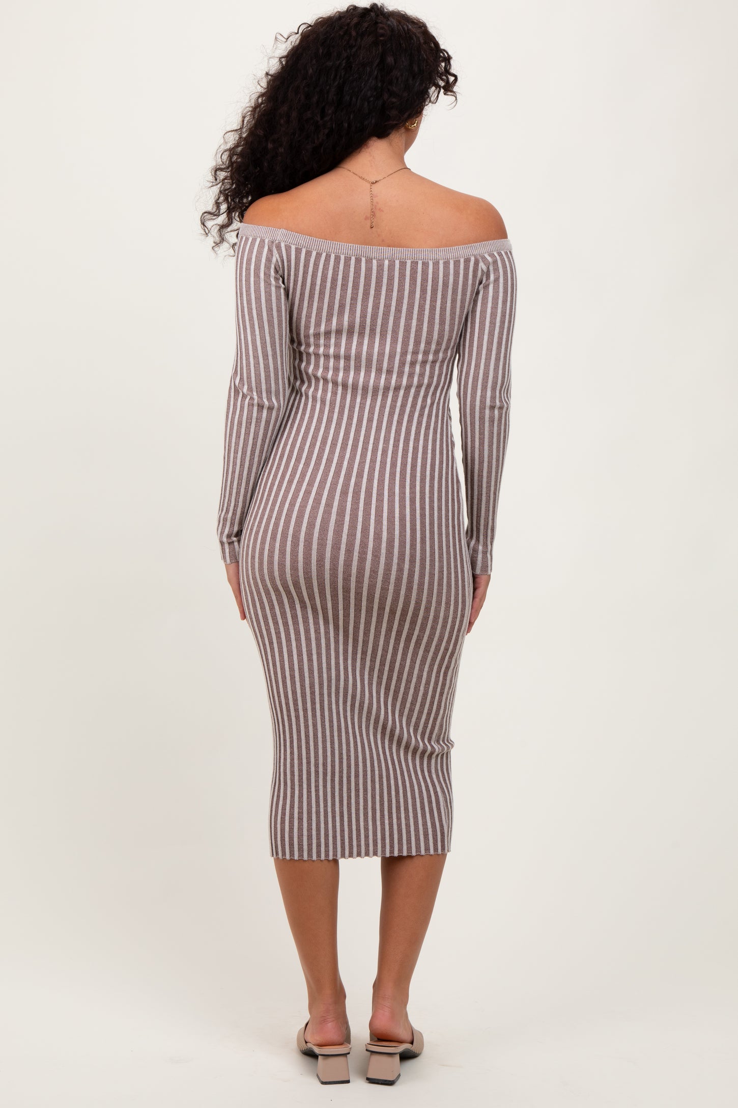woman wearing a fitted off-the-shoulder striped midi dress in brown and beige, showing a form-fitting silhouette from the back