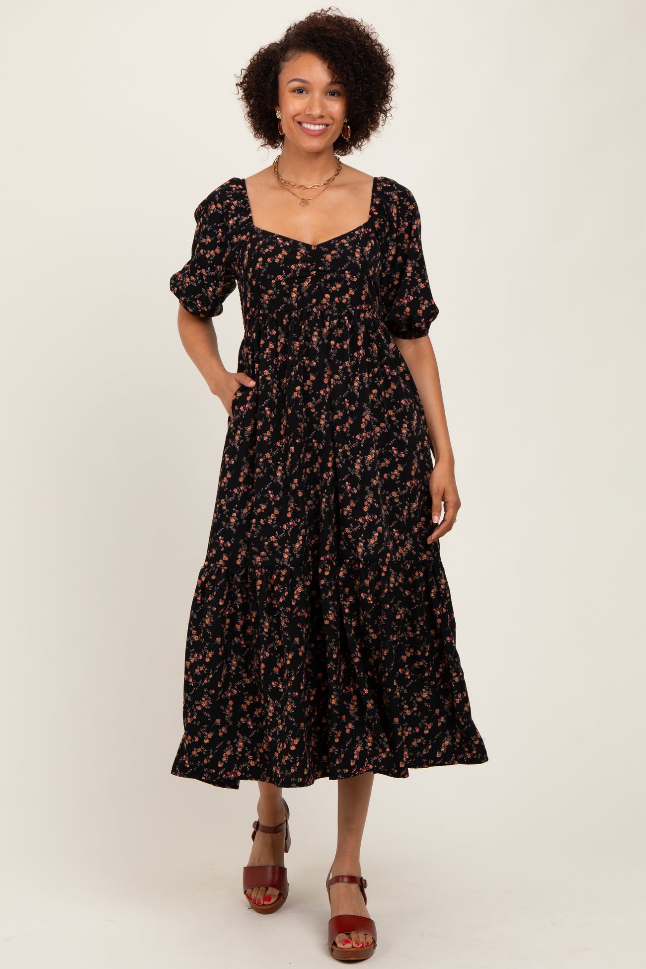 woman wearing a black floral maxi dress with puff sleeves and a square neckline, standing and smiling