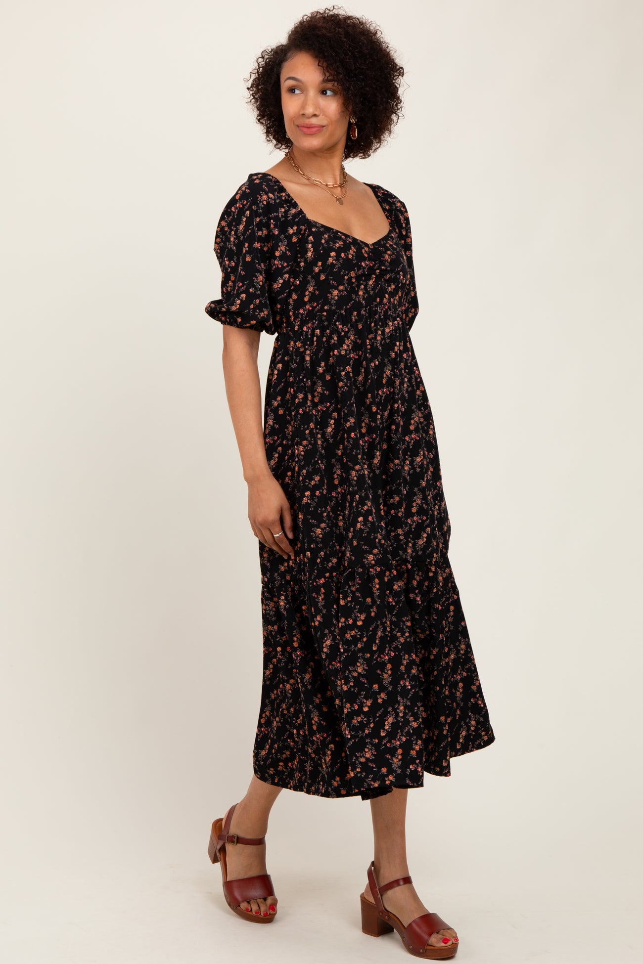 woman wearing a black floral midi dress with puff sleeves and a tiered skirt, paired with brown strappy sandals