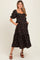 woman wearing a black floral print maternity dress with puff sleeves and pockets, standing with a baby bump visible