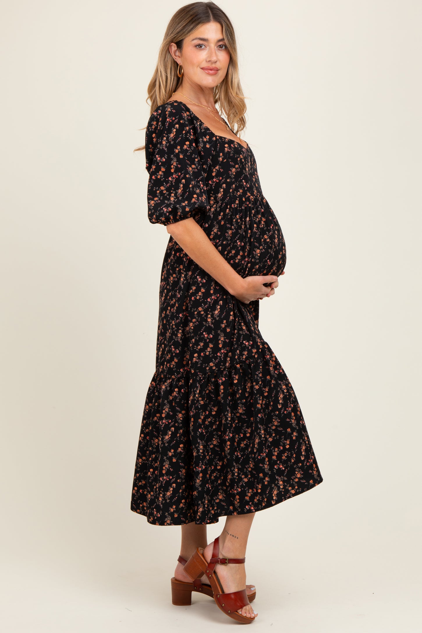 woman wearing a black floral maternity dress with a ruffled hem and holding her baby bump
