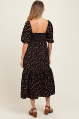 woman wearing a black floral print maternity dress with puff sleeves and a tiered skirt, showing her back