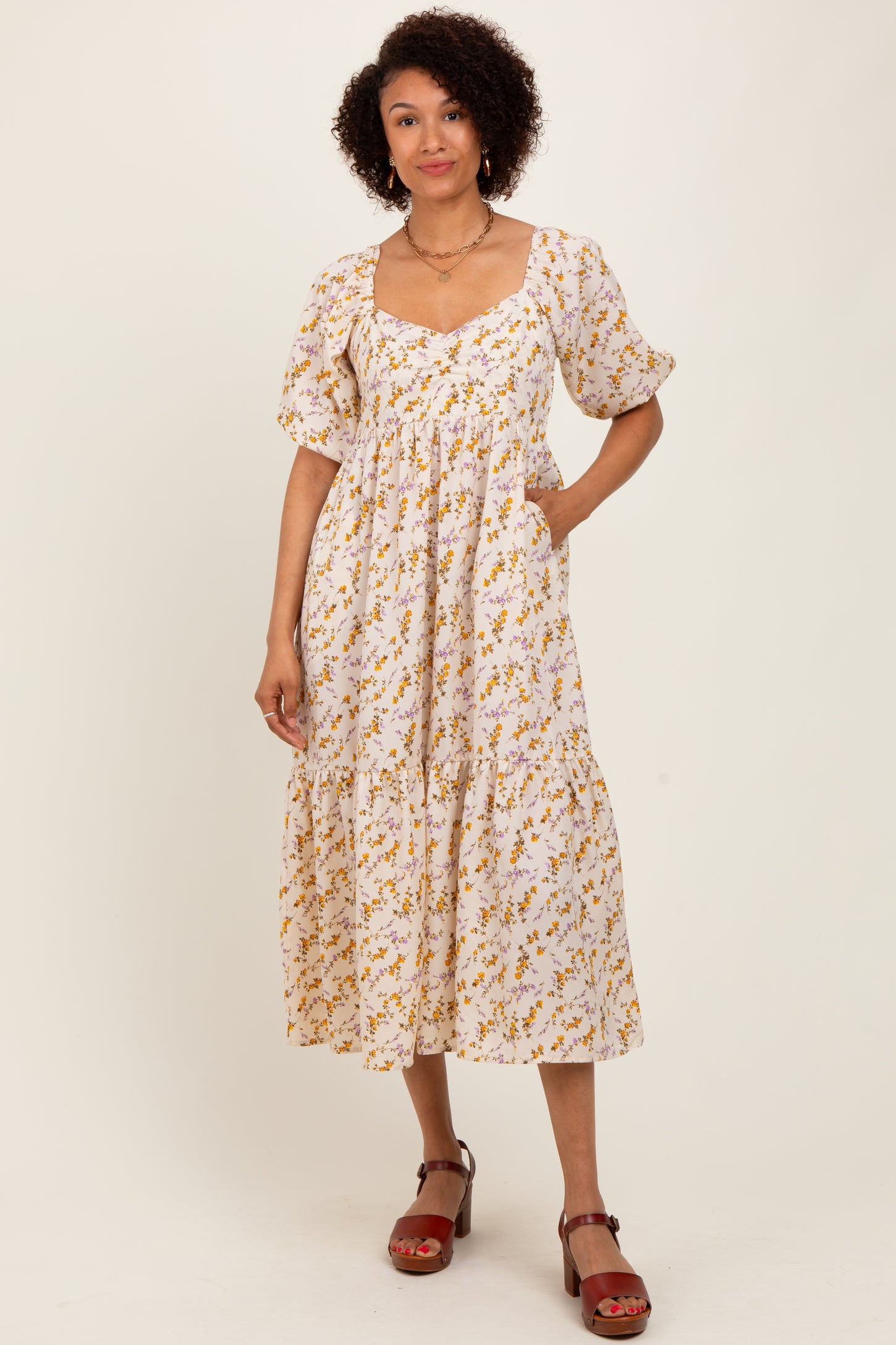 woman wearing a white floral midi dress with puff sleeves and pockets, standing against a plain background