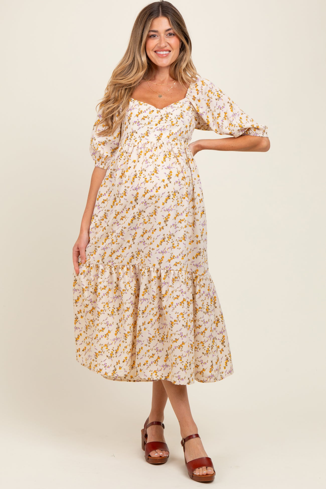 woman wearing a white floral maternity dress with puffed sleeves and a tiered hem, showing her baby bump