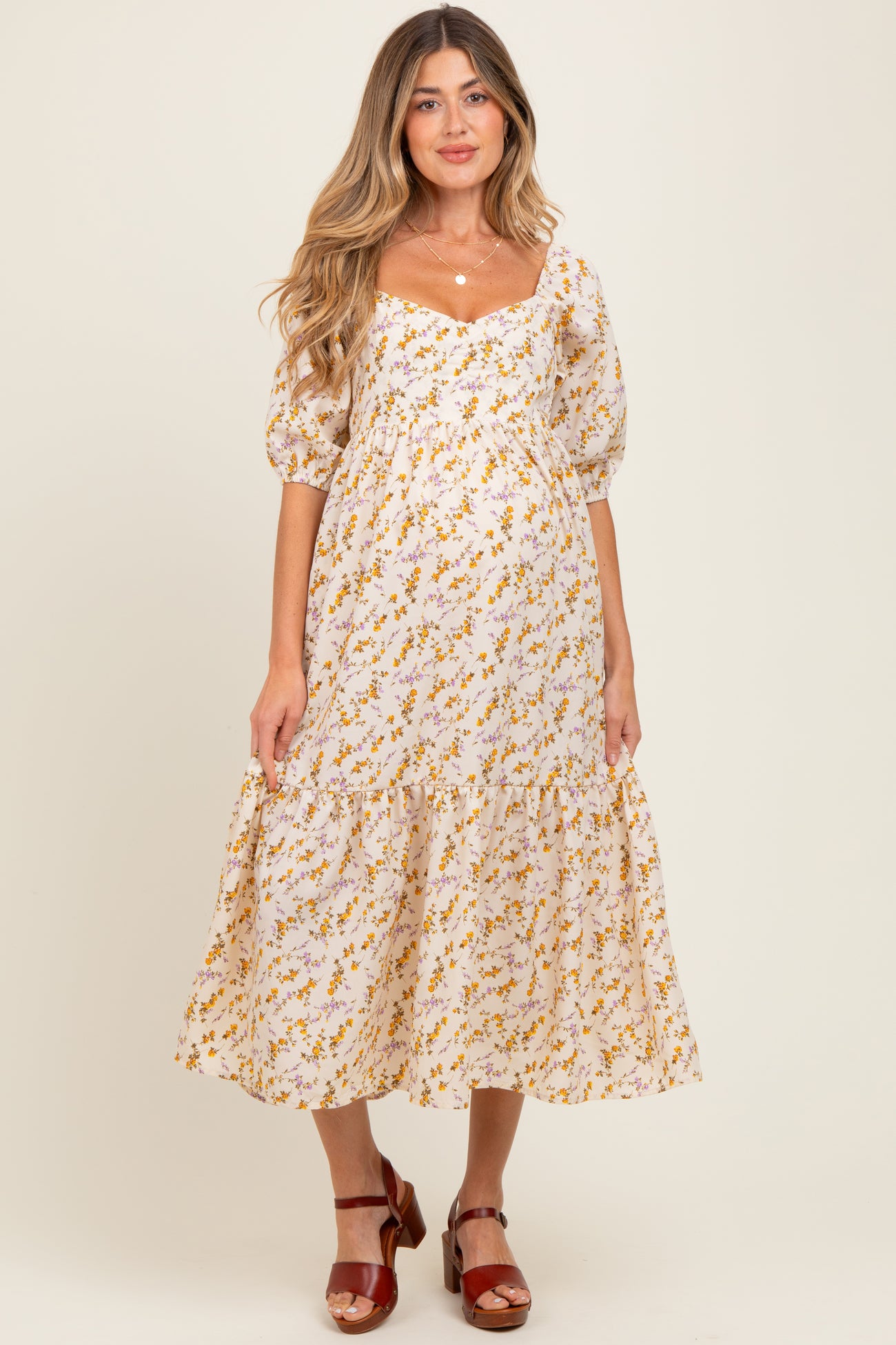 woman wearing a floral maternity dress with puffed sleeves and a tiered skirt, showcasing her baby bump