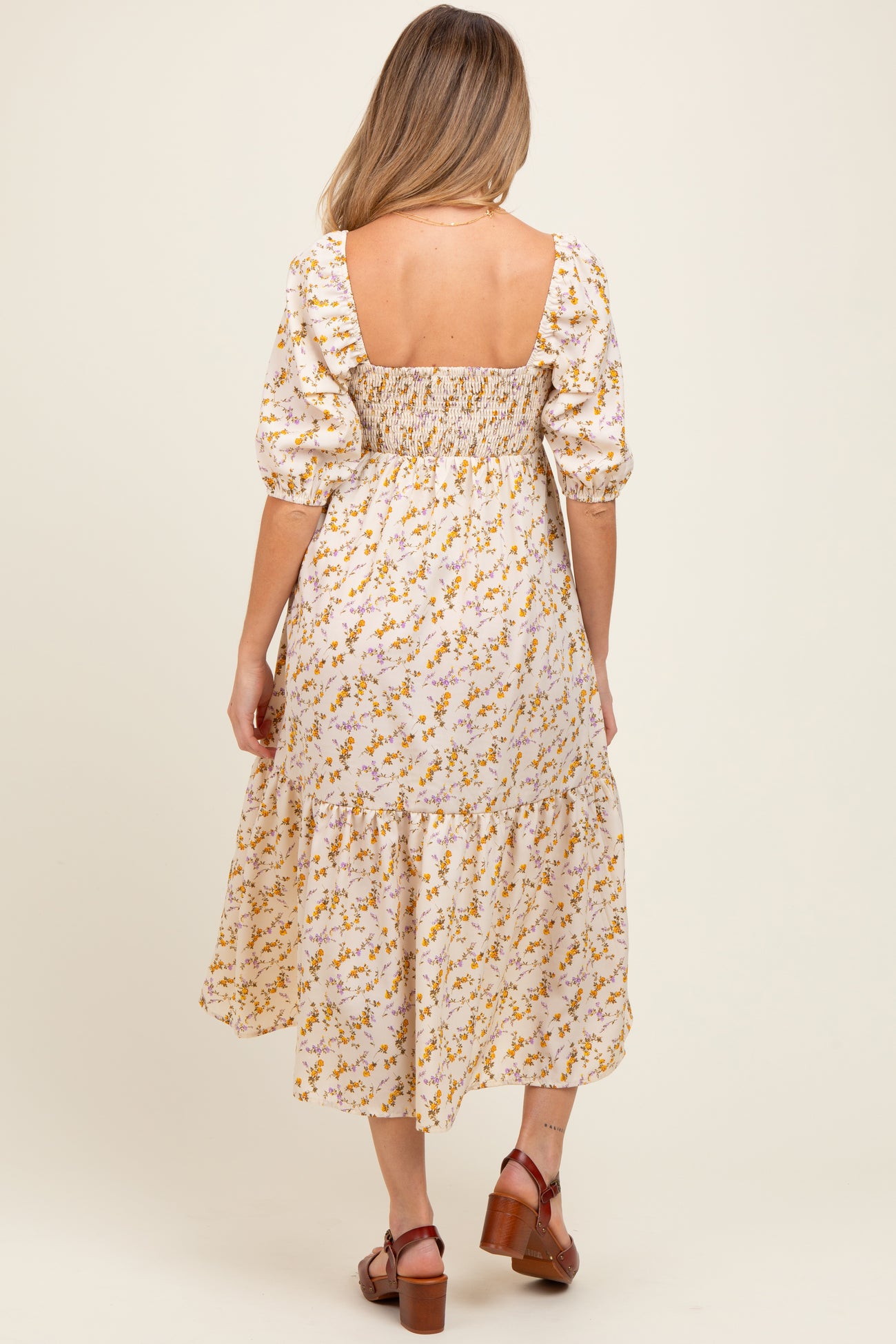 woman wearing a floral maternity dress with puff sleeves and a tiered skirt, highlighting a baby bump from the back