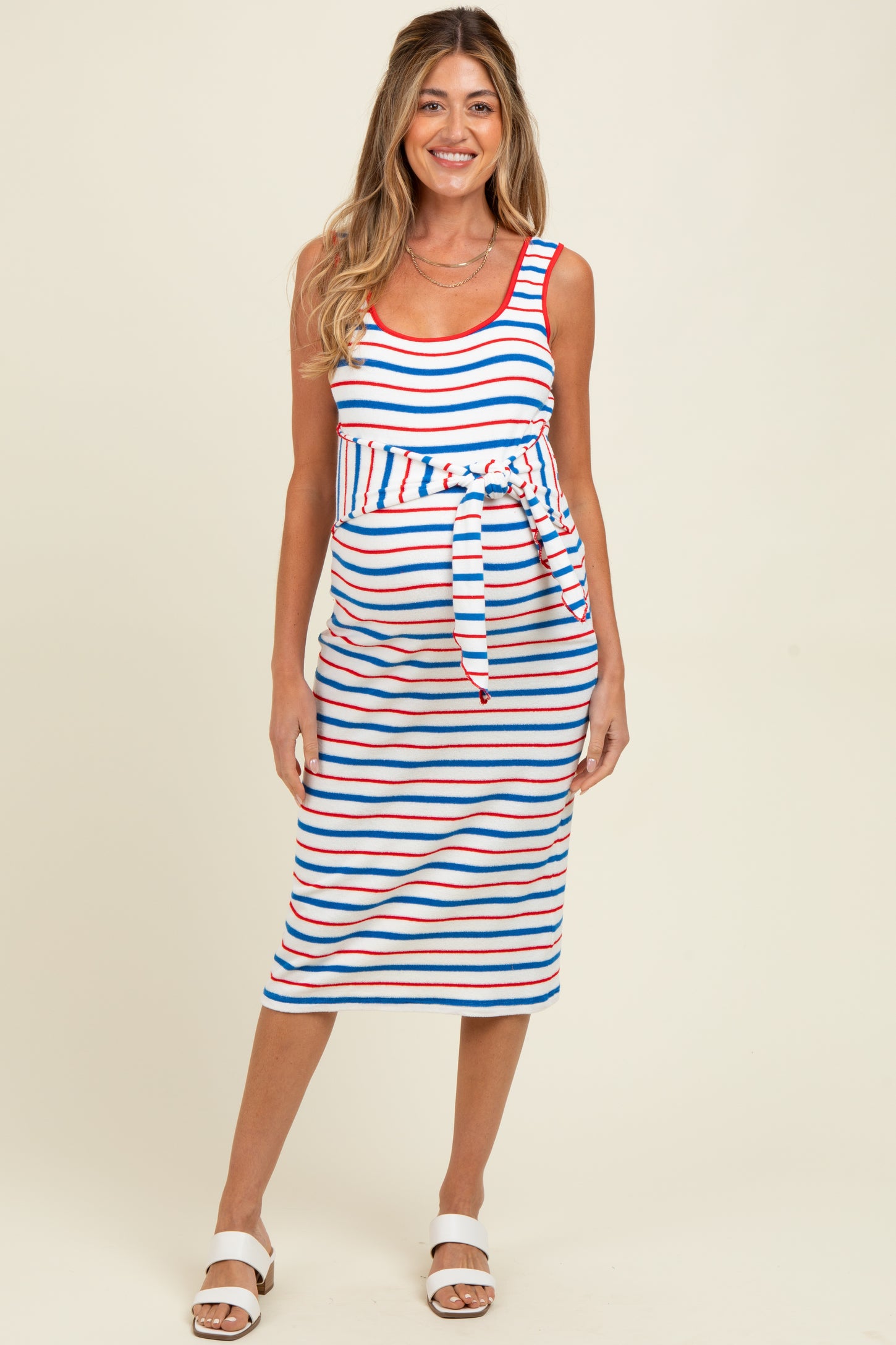woman wearing a striped maternity dress with a tie waist, featuring red, blue, and white stripes and a visible baby bump