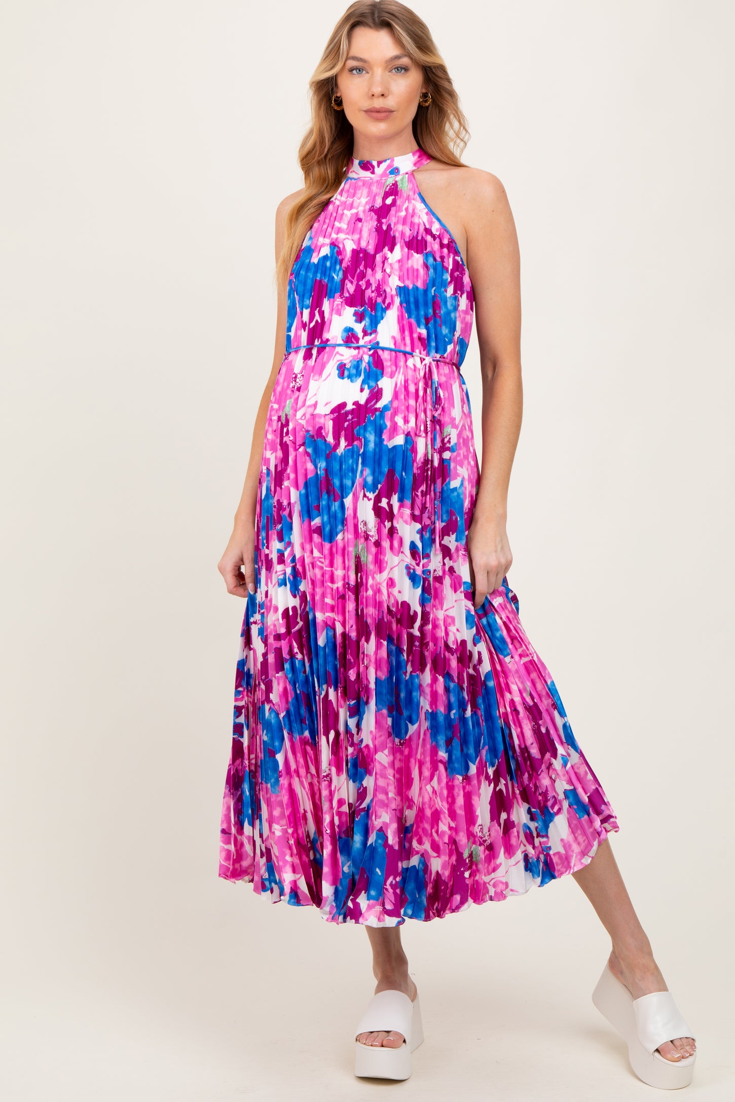 woman wearing a colorful floral print maternity dress with a halter neckline and flowing pleated skirt, baby bump visible