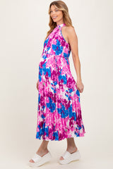 woman wearing a colorful floral print maternity dress with a halter neckline and a flowing skirt, showing her baby bump