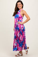woman wearing a pink and blue floral maxi dress with a halter neck and tie waist, standing on a light background