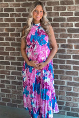 woman wearing a floral print maternity dress in pink and blue, cradling her baby bump against a brick wall