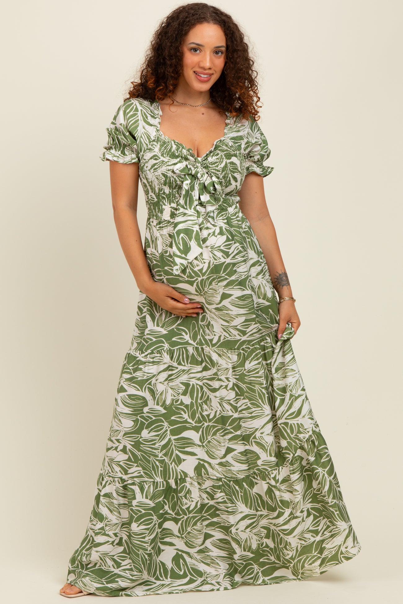 woman wearing a green floral maternity maxi dress and cradling her baby bump