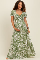 woman wearing a green floral maternity maxi dress and cradling her baby bump