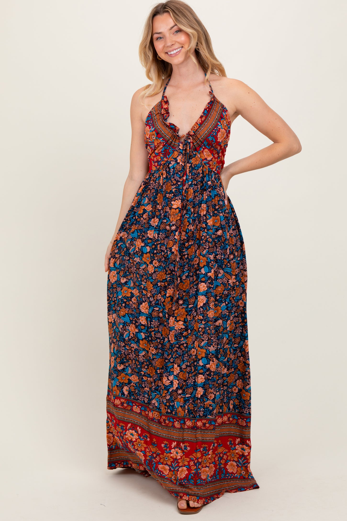 woman wearing a floral halter maxi dress in navy, orange, and red with a tie front and flowing skirt