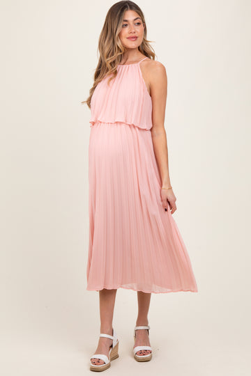 woman wearing a blush pink pleated maternity dress with a flowing halter neckline and visible baby bump