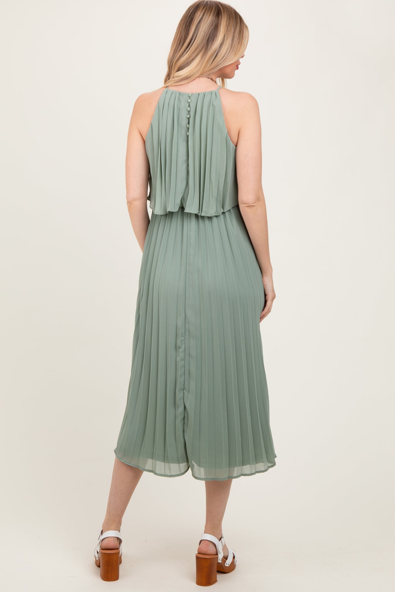 woman wearing a back view of a pleated sage green midi dress with a halter neckline and layered top