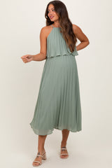 woman wearing a light green pleated maternity dress with a halter neck and flowing silhouette, showing her baby bump