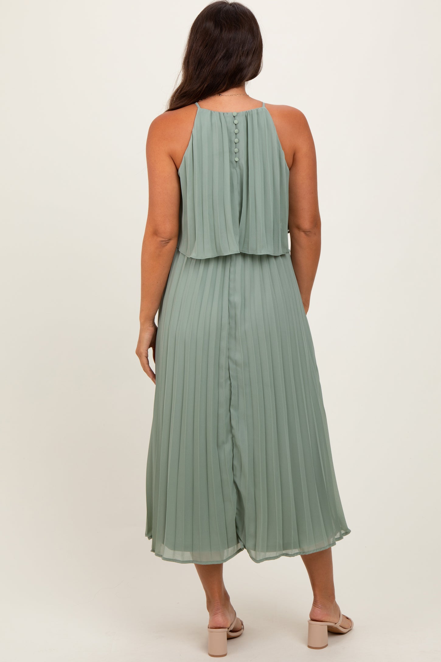 woman wearing a light green pleated maternity dress with a sleeveless design and button details at the back