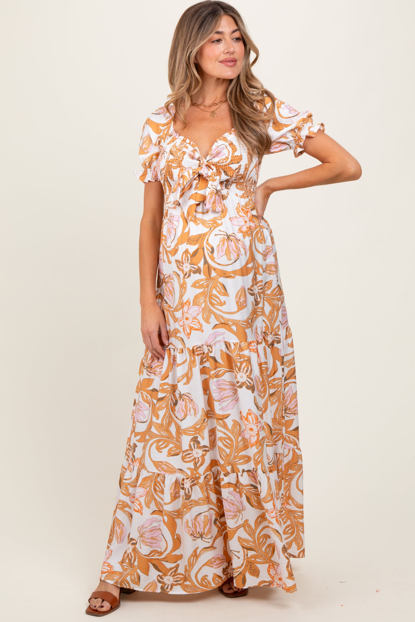 woman wearing a floral print orange and white maxi maternity dress with short ruffled sleeves and a smocked bodice