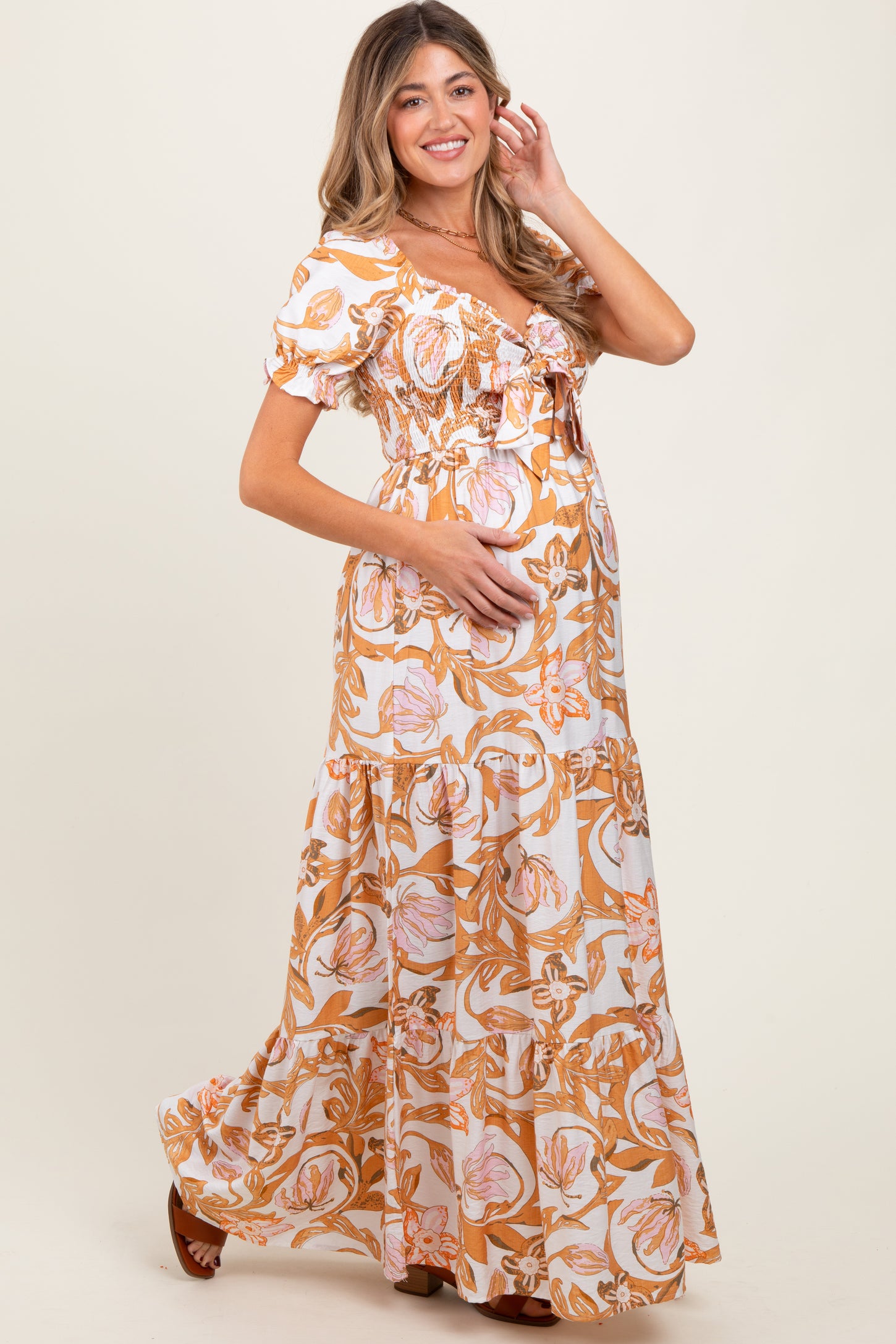 woman wearing a floral maternity maxi dress with puff sleeves and a baby bump, smiling and posing with one hand on her hip