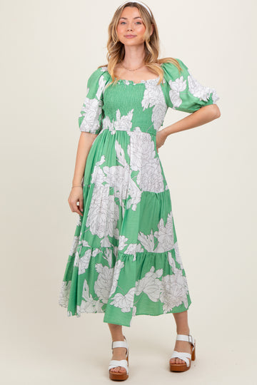 woman wearing a green floral midi dress with puff sleeves and smocked bodice, standing and smiling