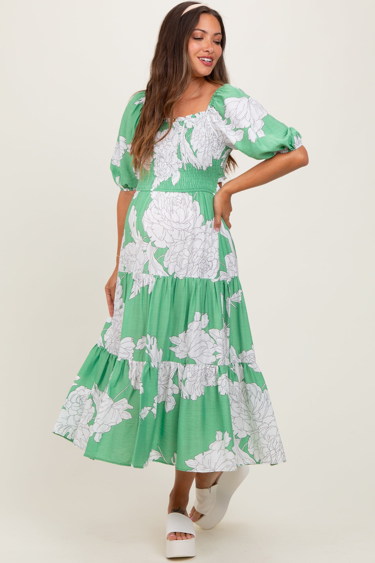 woman wearing a green floral maternity dress with short puff sleeves and a tiered skirt, posing outdoors