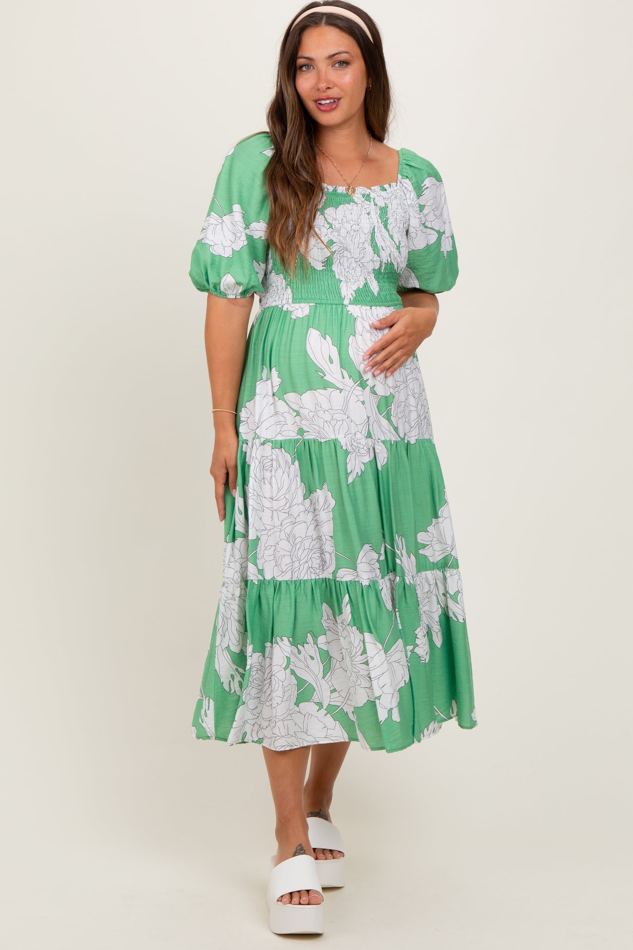 woman wearing a green floral maternity dress with puffed sleeves and a baby bump visible