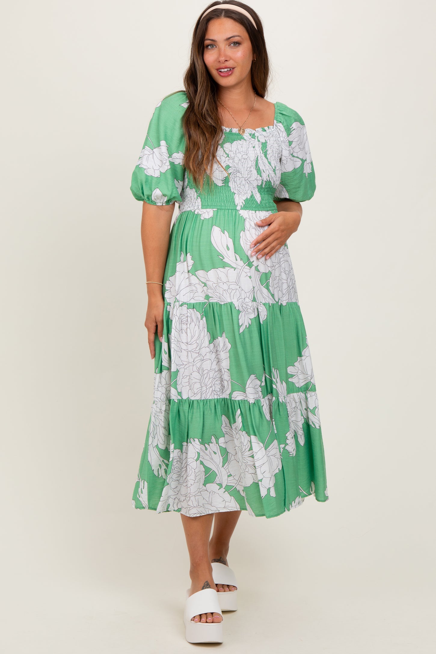woman wearing a green floral maternity dress with puffed sleeves and a baby bump visible