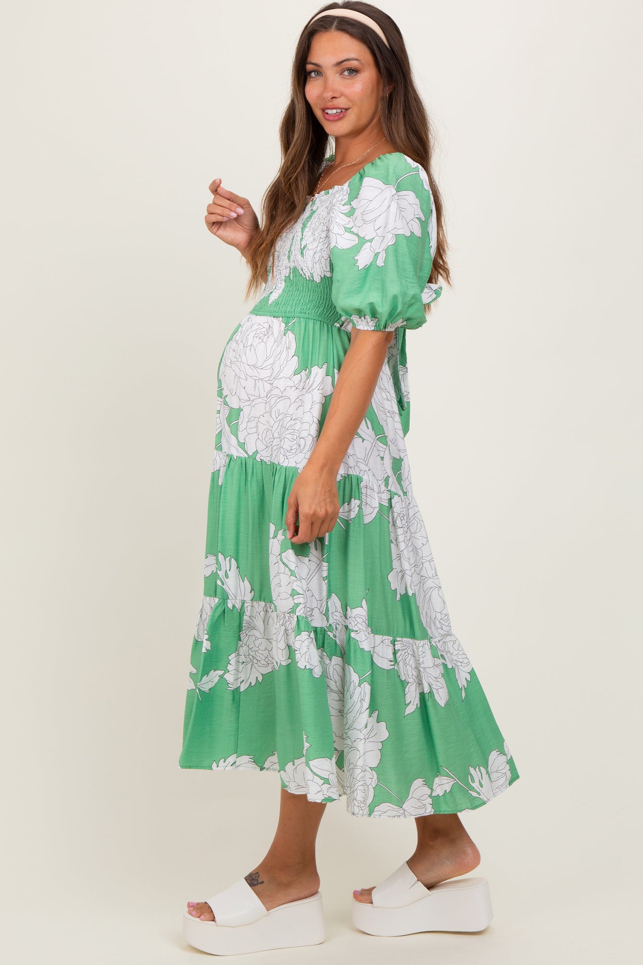 woman wearing a green floral maternity dress with puff sleeves and tiered skirt, showing her baby bump