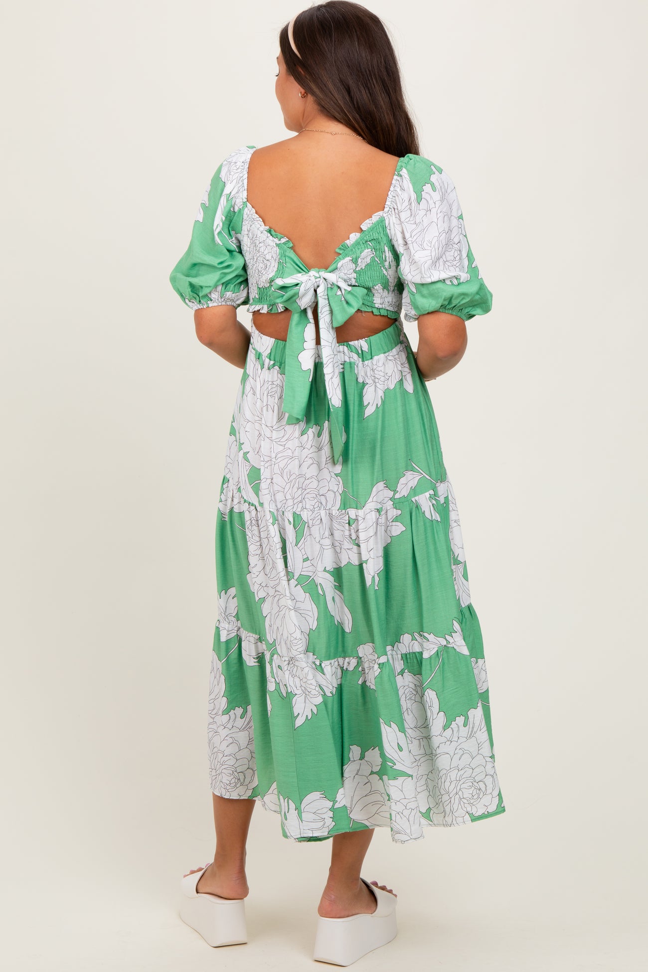 woman wearing a green floral maternity maxi dress with puff sleeves and an open back detail