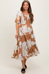 woman wearing a brown maternity dress with white floral print and puff sleeves, smiling and standing against a neutral background