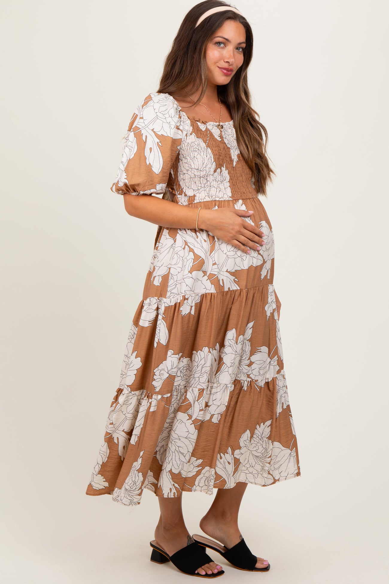 woman wearing a brown floral maternity dress with puff sleeves and holding her baby bump