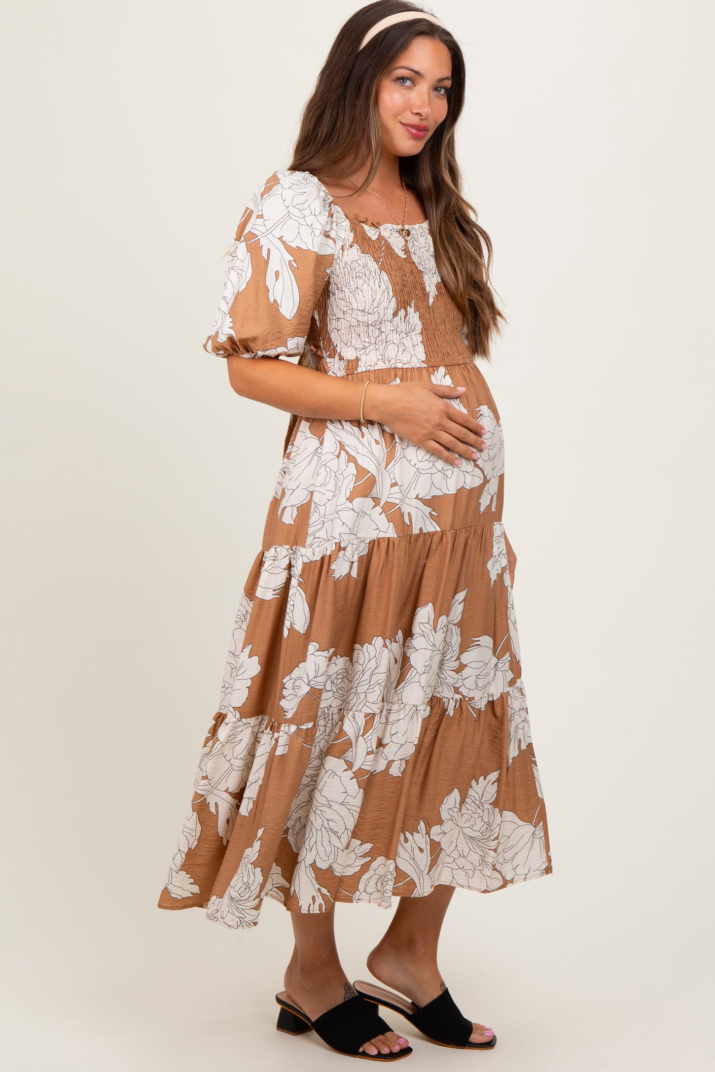 woman wearing a brown floral maternity dress with puff sleeves and holding her baby bump