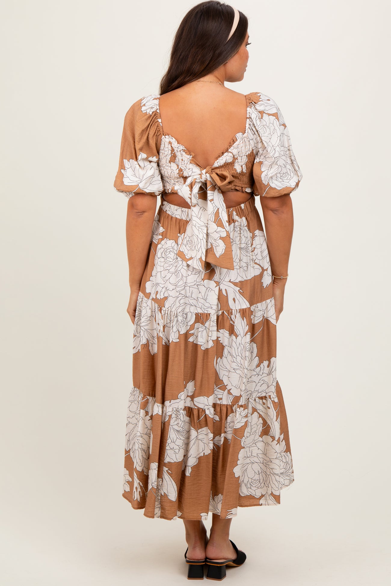 woman wearing a brown floral print maternity maxi dress with puff sleeves and open back detail