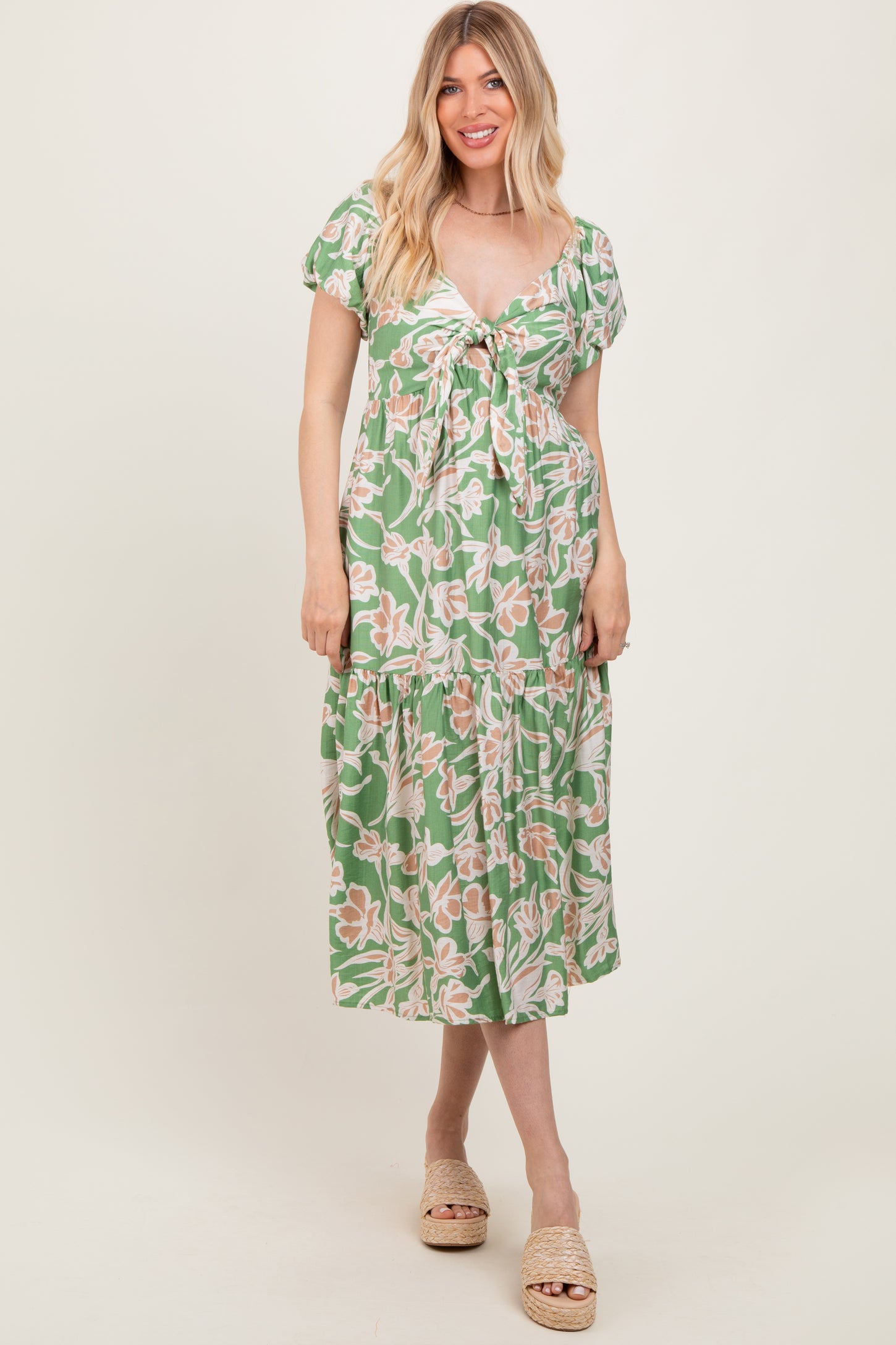 woman wearing a green floral midi dress with a tie front and puff sleeves, standing and smiling