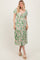 woman wearing a green floral midi dress with a tie front and puff sleeves, standing and smiling
