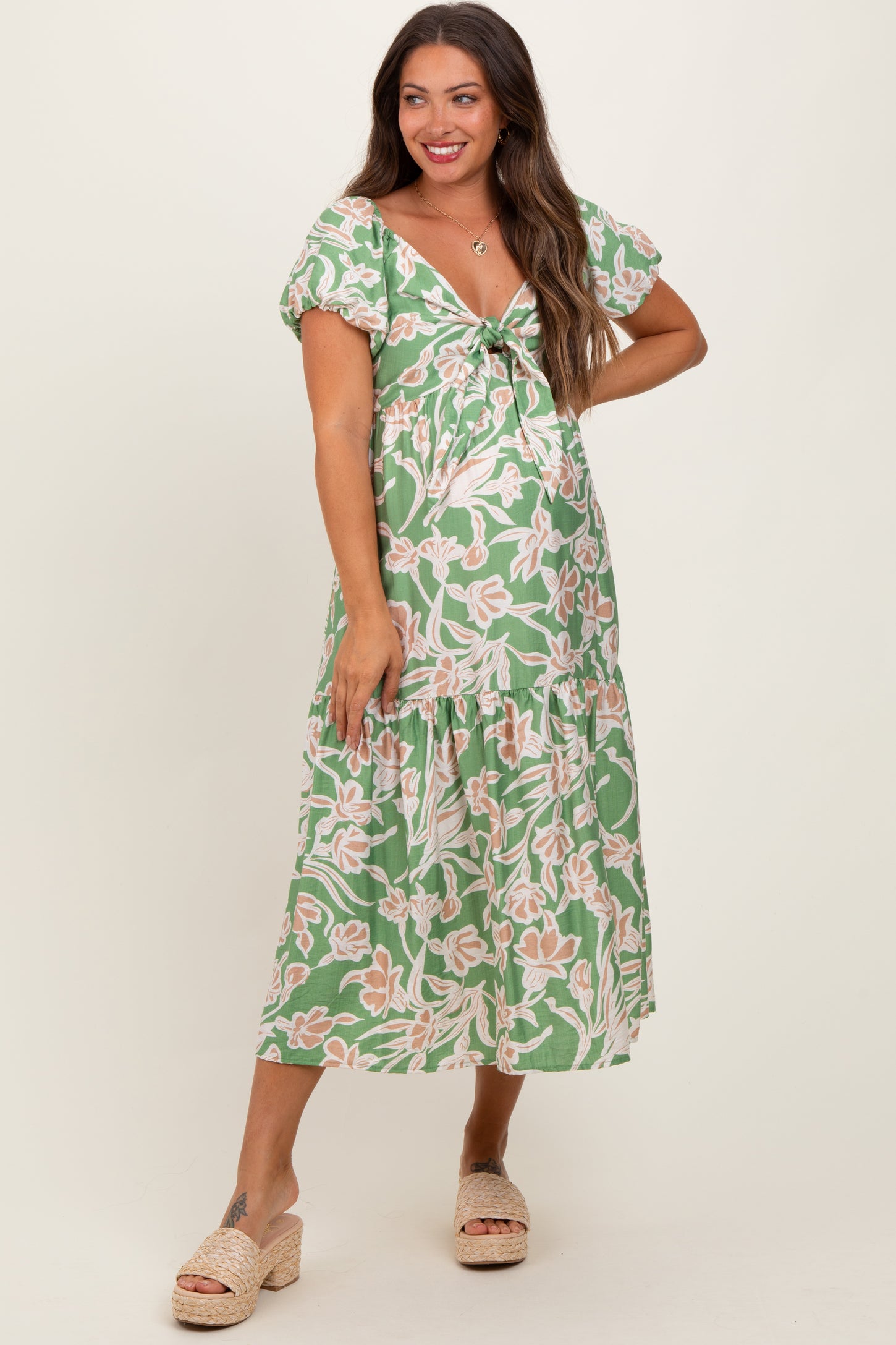 woman wearing a green floral maternity dress with puff sleeves and a tie-front detail, showcasing her baby bump