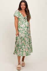 woman wearing a green floral maternity dress with a v-neckline and tiered skirt, showing her baby bump