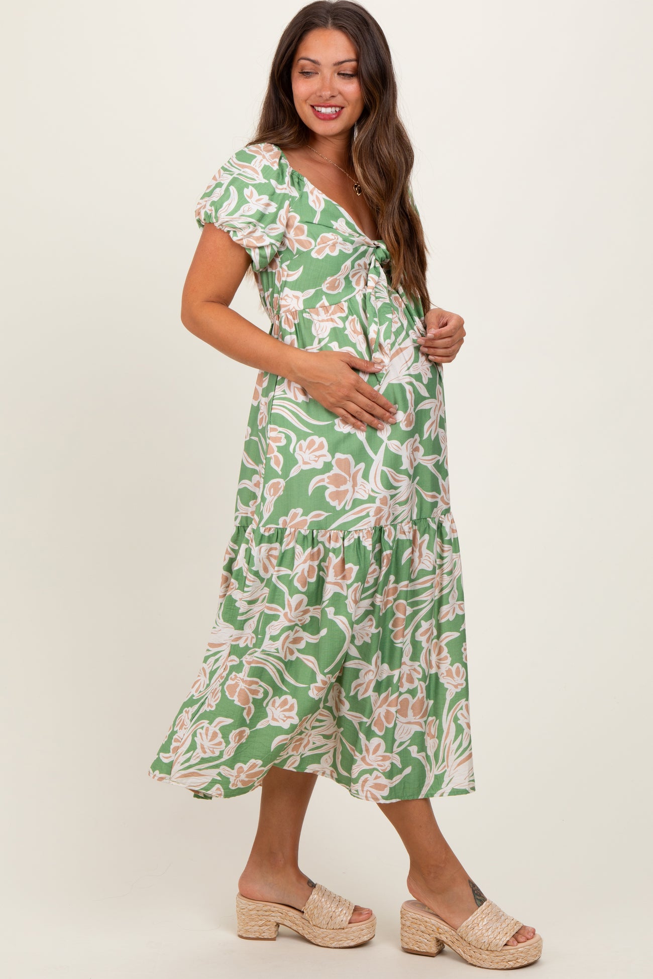 woman wearing a green floral maternity dress with puff sleeves and holding her baby bump