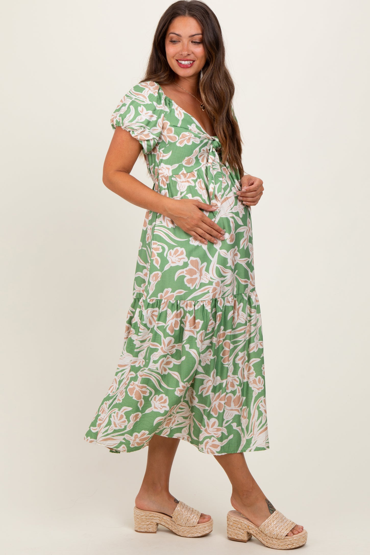 woman wearing a green floral maternity dress with puff sleeves and holding her baby bump