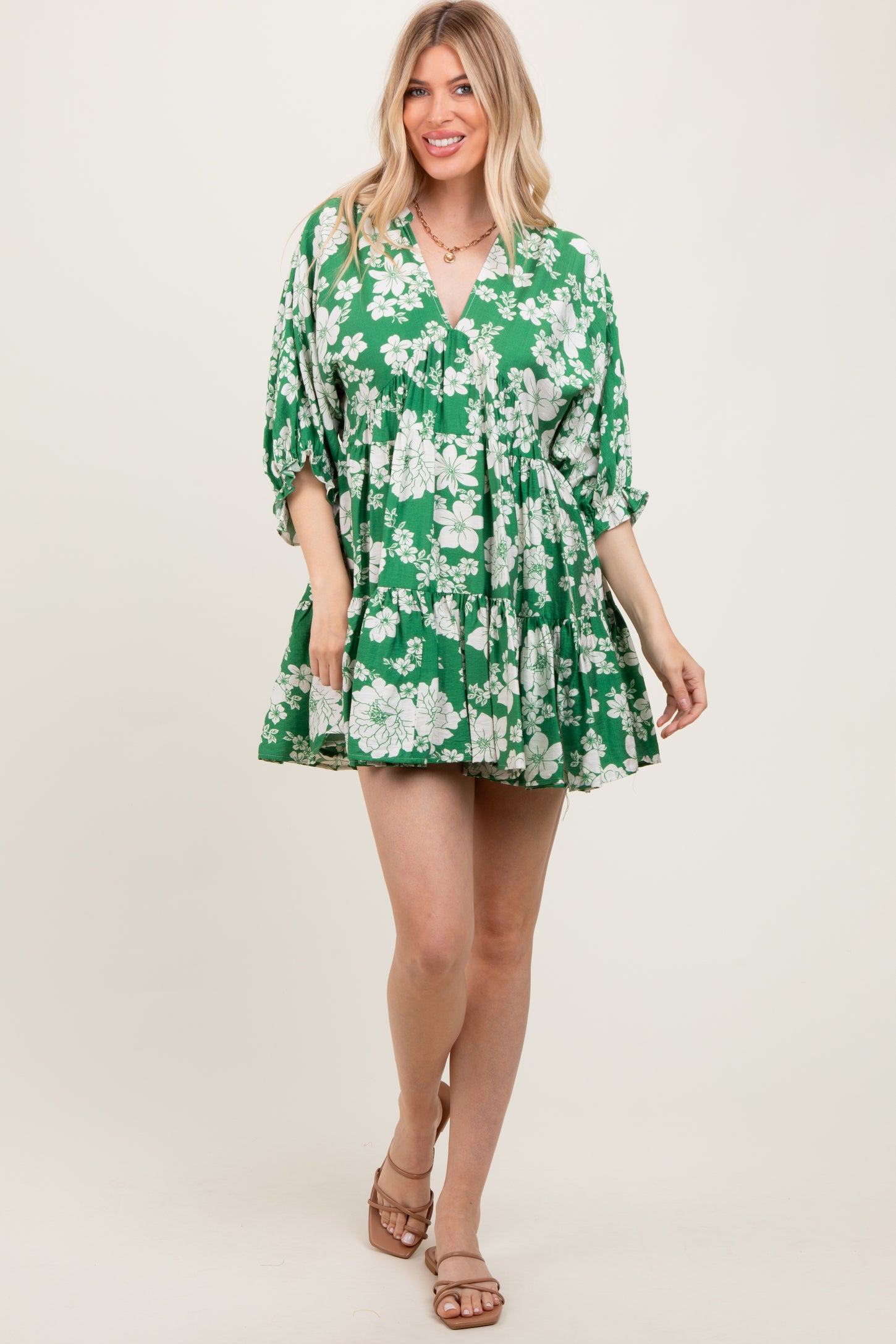 woman wearing a green floral mini dress with a v-neck and tiered skirt, standing and smiling