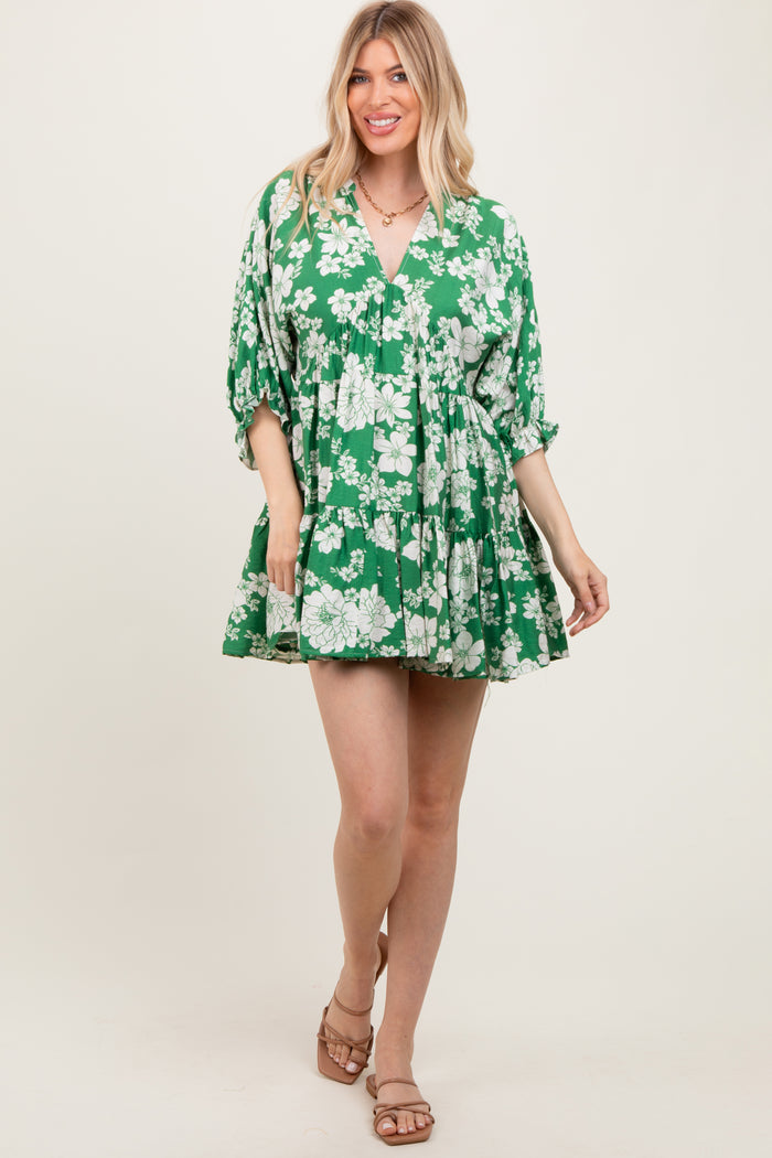 woman wearing a green floral mini dress with a v-neck and tiered skirt, standing and smiling