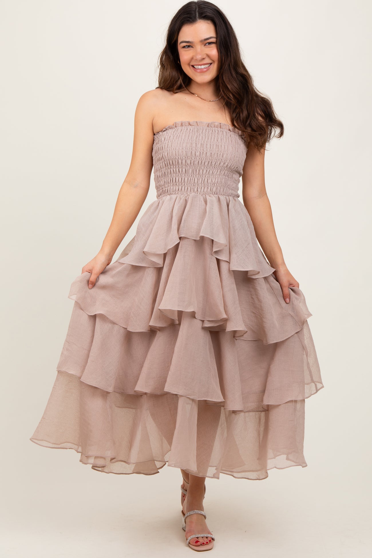 woman wearing a strapless light beige tiered maxi dress with a fitted bodice and ruffled layers