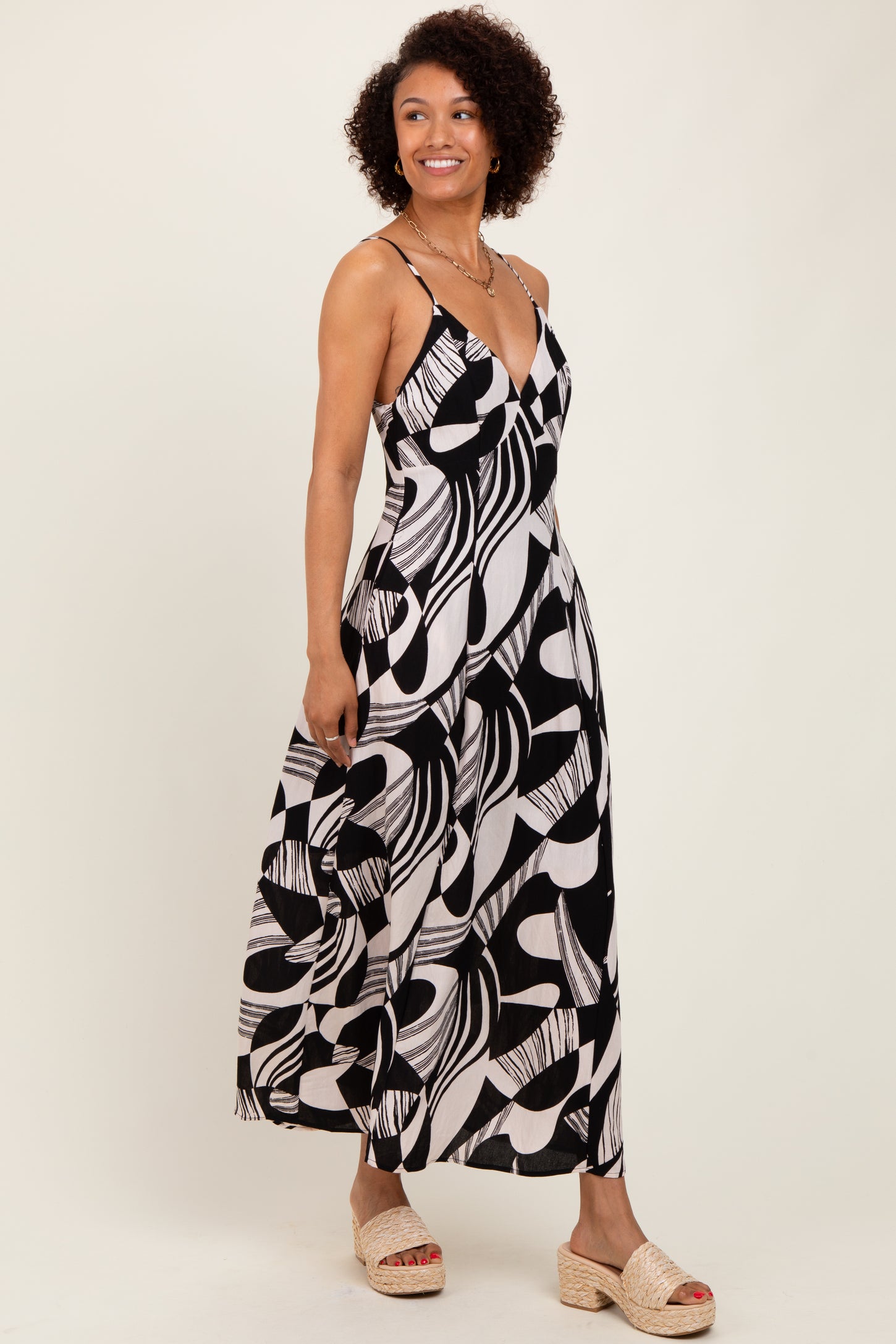 woman wearing a black and white patterned maxi dress with spaghetti straps and a V-neckline, standing sideways